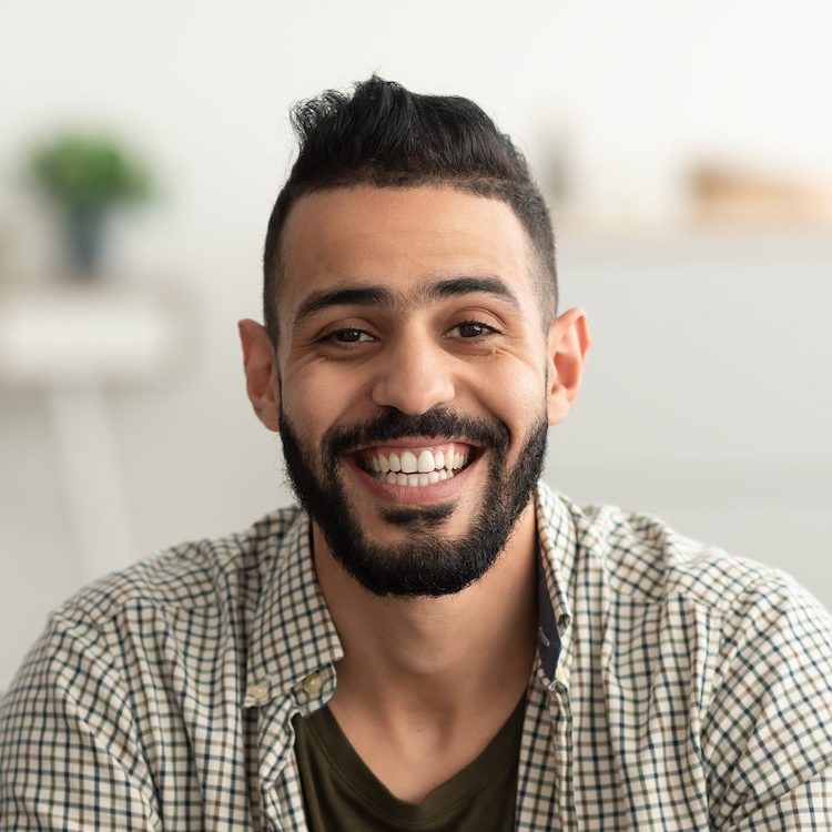 portrait of handsome young arab man smiling and looking at camera sitting on sofa at home e1682562032200
